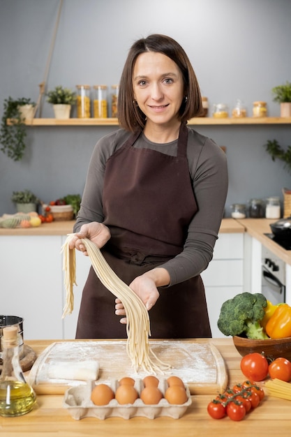 Felice giovane donna caucasica in grembiule che prepara spaghetti