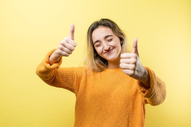 Felice giovane donna caucasica in un maglione arancione che fa segno con il pollice e sorridente Buon lavoro e rispetto