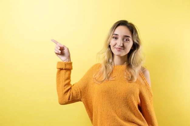 Felice giovane donna caucasica in un maglione giallo che punta le dita lontano.