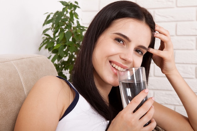 Felice giovane donna che beve acqua a casa