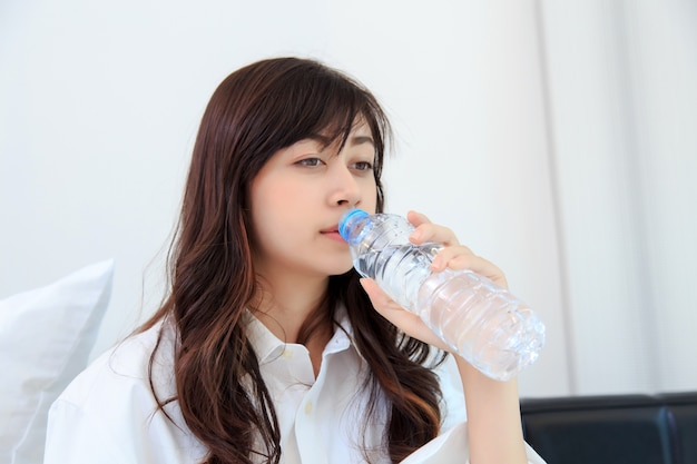 felice giovane donna che beve acqua pura nella sua camera da letto. concetto per sano.