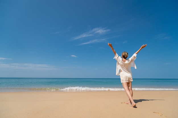 Felice giovane donna che gode della libertà con le mani aperte sul mare.