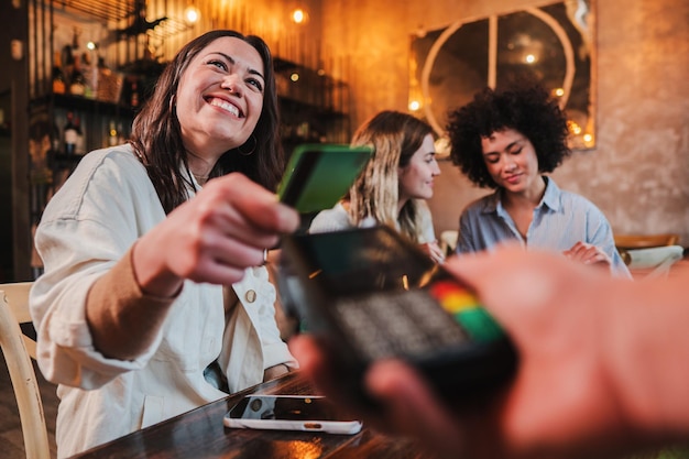 Felice giovane donna che paga il conto con una carta di credito senza contatto in un ristorante Donna sorridente che tiene una carta di credito e dà una transazione di pagamento al cassiere