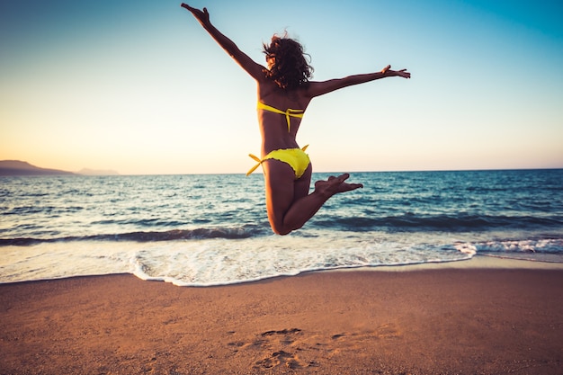 Felice giovane donna che salta sulla spiaggia