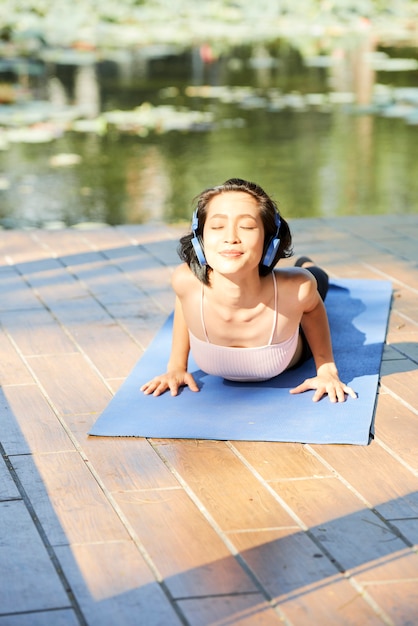 Felice giovane donna che si gode la mattinata di sole e ascolta la musica in cuffia quando si fa cobra asana all'aperto