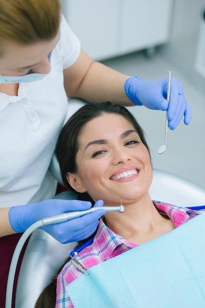 Felice giovane donna che sorride mentre una dentista in una maschera medica tiene gli strumenti vicino alla sua bocca