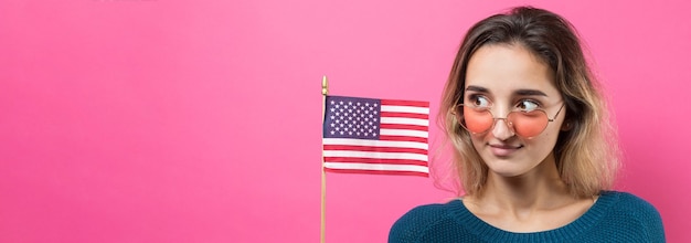 Felice giovane donna che tiene bandiera americana su uno sfondo rosa da studio