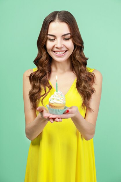 Felice giovane donna che tiene cupcake di compleanno con una candela sulla parete a colori