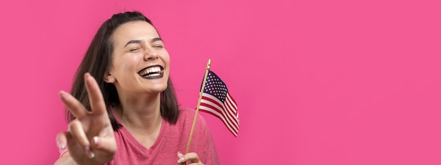 Felice giovane donna che tiene la bandiera americana su uno sfondo rosa da studio