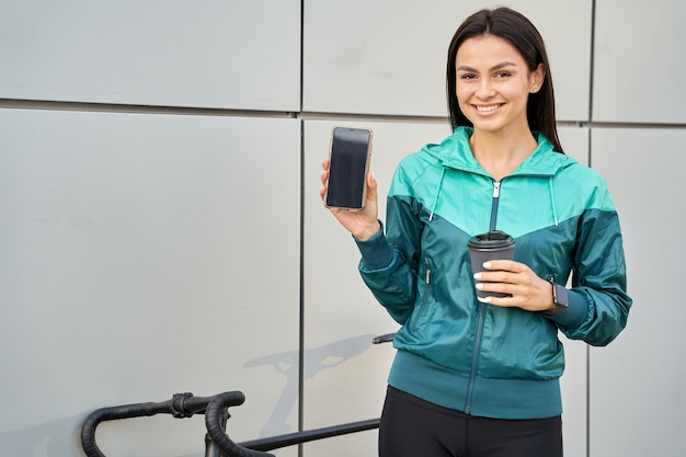 Felice giovane donna che tiene telefono cellulare e bevanda calda con la bici sullo sfondo. Copia spazio