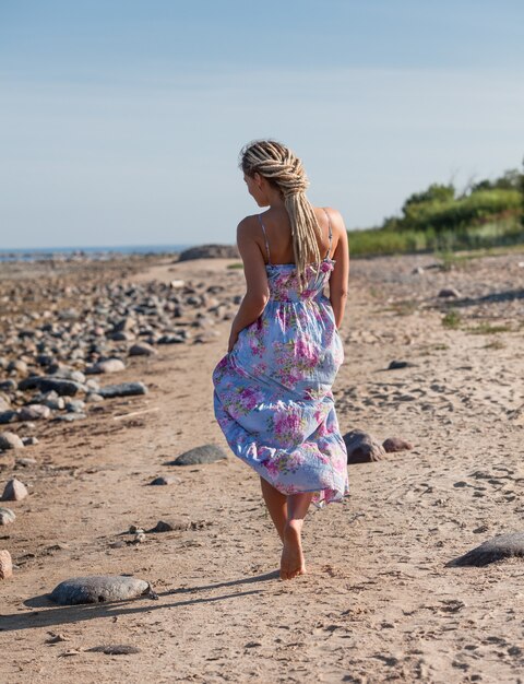 Felice giovane donna con i dreadlocks che cammina lungo la riva del mare