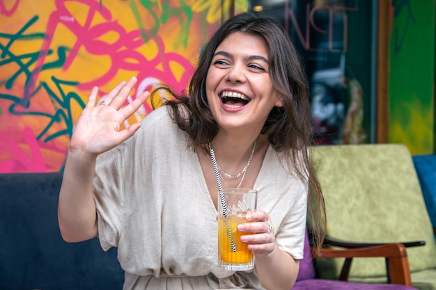 Felice giovane donna con un bicchiere di limonata contro un muro dipinto luminoso