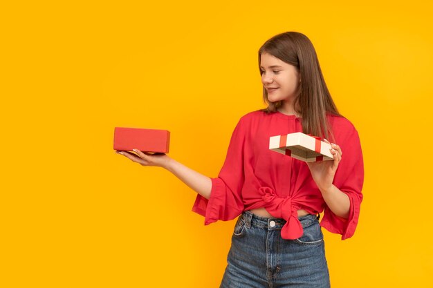 Felice giovane donna con una confezione regalo aperta e guarda dentro Ragazza sorridente ha ricevuto un regalo Sfondo giallo