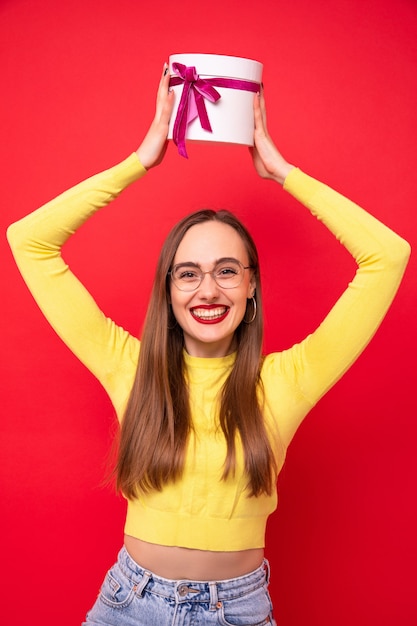 Felice giovane donna con una confezione regalo bianca su sfondo rosso