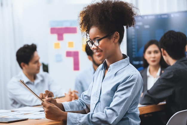 Felice giovane donna d'affari africana che indossa occhiali ritratto con un gruppo di impiegati in una riunione con schermo business dashboard sullo sfondo Donna d'ufficio sicura alla riunione di squadra Concord