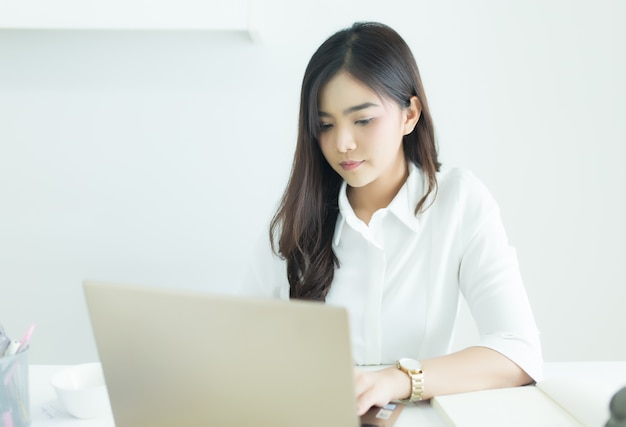 Felice giovane donna d&#39;affari asiatici che lavora sul suo computer portatile sul posto di lavoro.