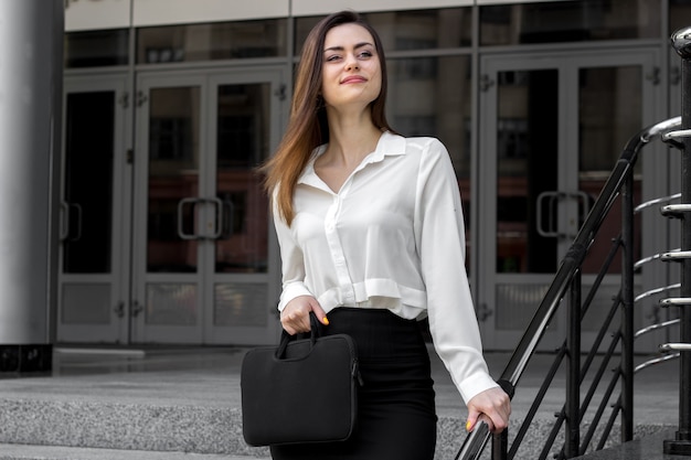 Felice giovane donna d'affari in piedi sulla strada e tenendo una borsetta nera