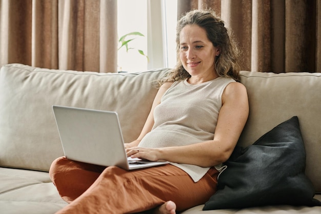 Felice giovane donna d'affari incinta o libero professionista femminile che digita sul computer portatile