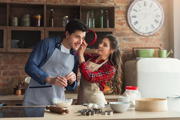 Felice giovane donna e uomo che cuociono la torta e si divertono in cucina a soppalco. Giovane famiglia che cucina a casa, donna che condivide con le cuffie dell'uomo con musica, copia spazio