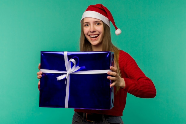 Felice giovane donna eccitata in cappello di babbo natale con scatola regalo su sfondo blu