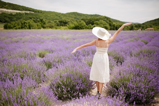 Felice giovane donna in abito bianco su campi di lavanda profumati in fiore con file infinite