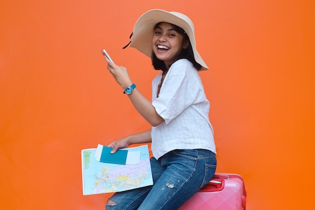 Felice giovane donna in cappello estivo utilizzando il telefono cellulare, tenendo passaporto e biglietti aerei. Giro di viaggio