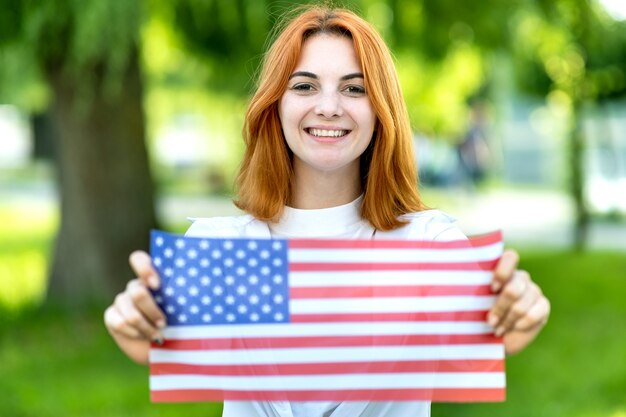 felice giovane donna in posa con la bandiera nazionale degli Stati Uniti tenendolo nelle sue mani tese