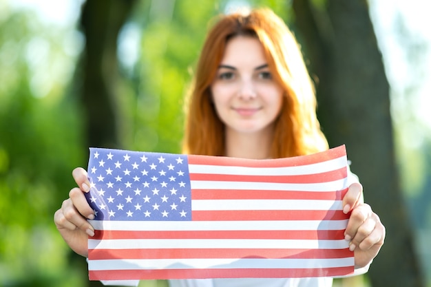 Felice giovane donna in posa con la bandiera nazionale Usa all'aperto nel parco