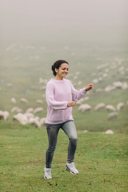 Felice giovane donna in un maglione contro mandrie di pecore in montagna in una giornata nebbiosa
