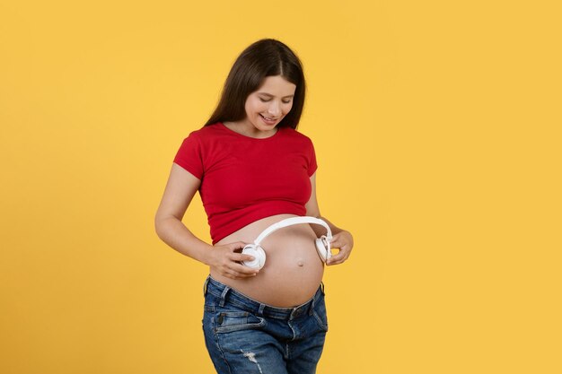 Felice giovane donna incinta che tiene le cuffie senza fili vicino alla pancia