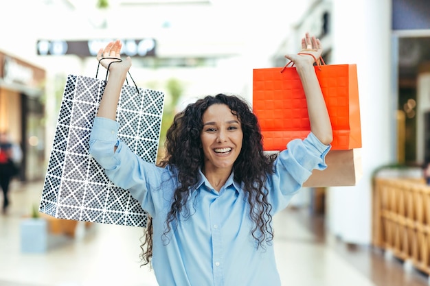 Felice giovane donna ispanica attraente che tiene i sacchetti della spesa colorati nelle sue mani nello shopping