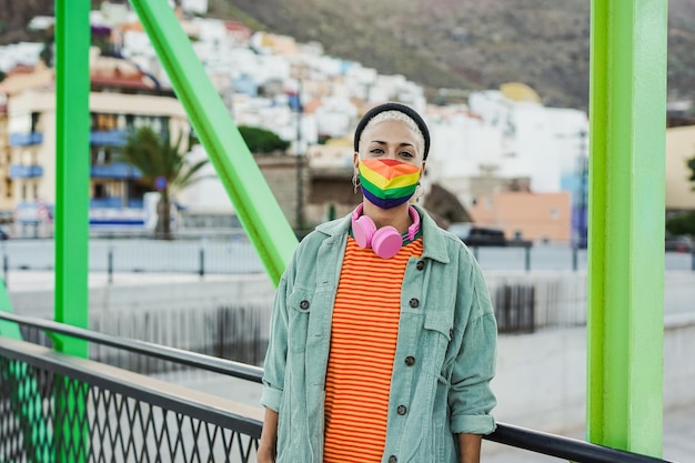 Felice giovane donna lesbica sorridente sulla fotocamera mentre indossa la maschera facciale arcobaleno LGBT