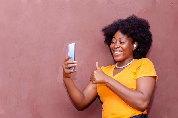 Felice giovane donna millenaria che effettua una videochiamata online utilizzando lo smartphone in piedi su uno sfondo marrone dello studio