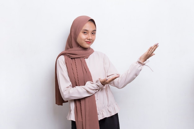 Felice giovane donna musulmana asiatica che punta con le dita in direzioni diverse su sfondo bianco