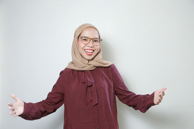 Felice giovane donna musulmana asiatica con gli occhiali che punta la mano in avanti isolato su sfondo bianco