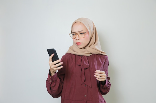 Felice giovane donna musulmana asiatica con gli occhiali utilizzando il telefono cellulare isolato su sfondo bianco