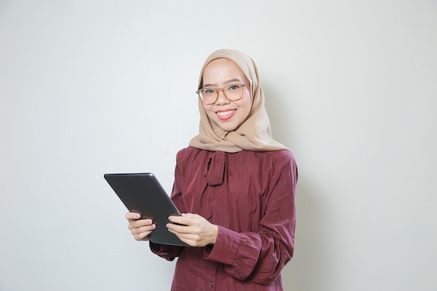 Felice giovane donna musulmana asiatica con gli occhiali utilizzando tablet su sfondo bianco isolato