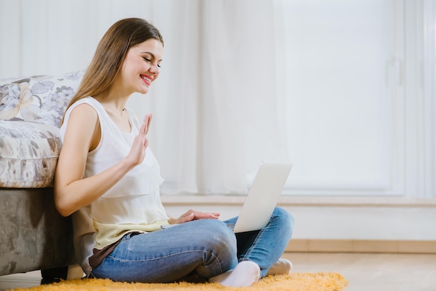 Felice giovane donna o studente con il computer portatile seduto sul pavimento a casa