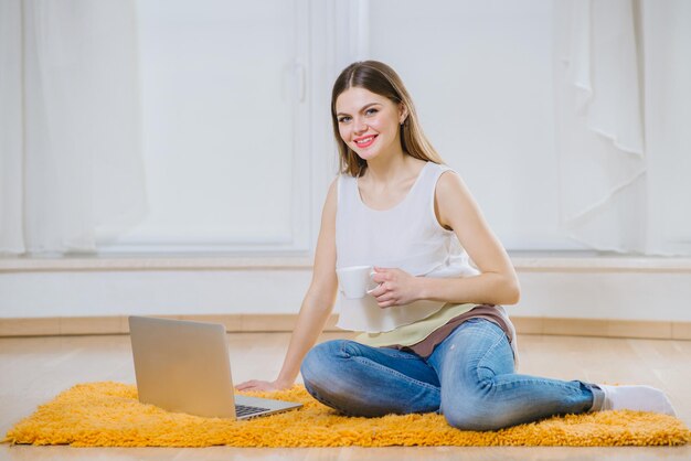 Felice giovane donna o studente con il computer portatile seduto sul pavimento a casa