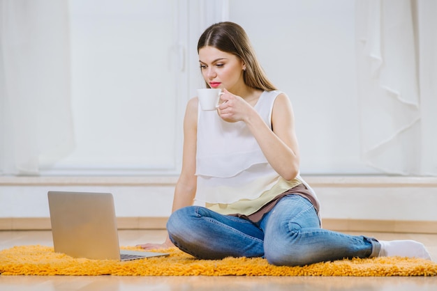 Felice giovane donna o studente con il computer portatile seduto sul pavimento a casa