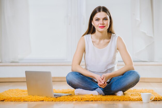 Felice giovane donna o studente con il computer portatile seduto sul pavimento a casa