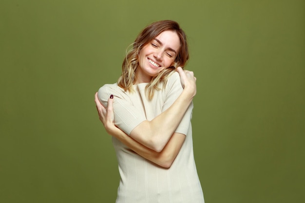 Felice giovane donna rilassata abbraccia se stessa sorridendo su sfondo verde amore per se stessi corpo per la cura di sé