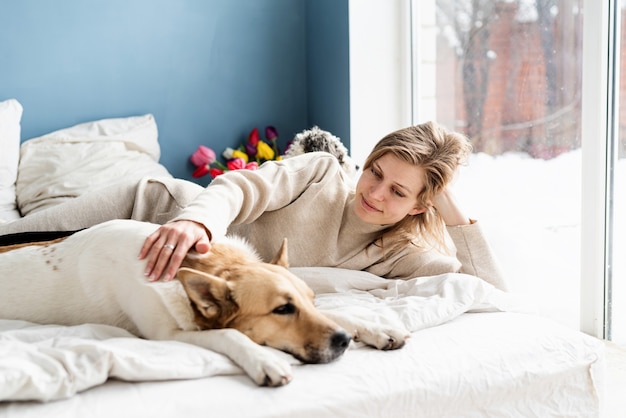 Felice giovane donna sdraiata a letto con i suoi cani, sfondo muro blu