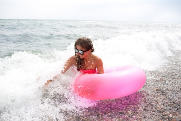 Felice giovane donna sedersi in riva al mare o oceano in onde con materasso ad aria rosa in mano e godere.