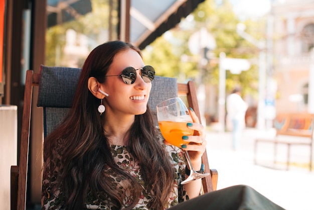 Felice giovane donna seduta all'aperto durante la giornata estiva e bevendo un bicchiere di limonata