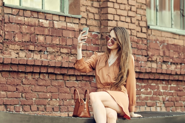 Felice giovane donna seduta su una panchina e facendo selfie con il telefono cellulare