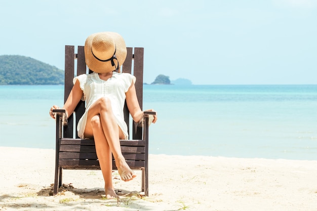 Felice giovane donna seduta sulla sedia a sdraio sulla spiaggia tropicale in abito bianco. Godersi la vita, umore estivo spensierato e rilassante