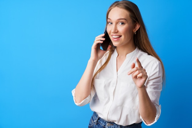 Felice giovane donna sorridente che parla al telefono su sfondo blu