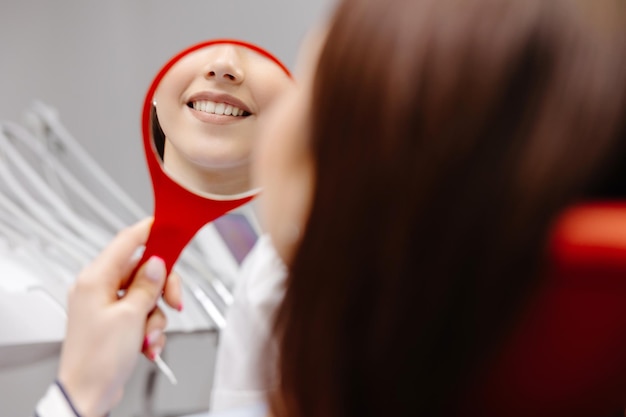 Felice giovane donna sorridente controllando i suoi denti sani perfetti nello specchio da vicino presso l'ufficio del dentista