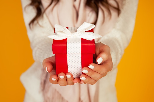 Felice giovane donna sorridente tenendo e tenendo il contenitore di regalo rosso davanti, offrendo e dando regali di Natale. Una ragazza con un maglione guarda e fa un regalo.